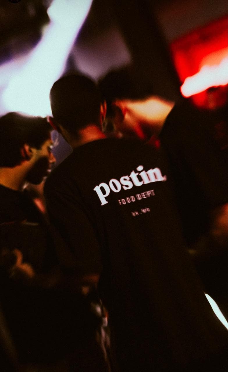 Convidados em evento Postin Food Dept, camiseta da marca em primeiro plano