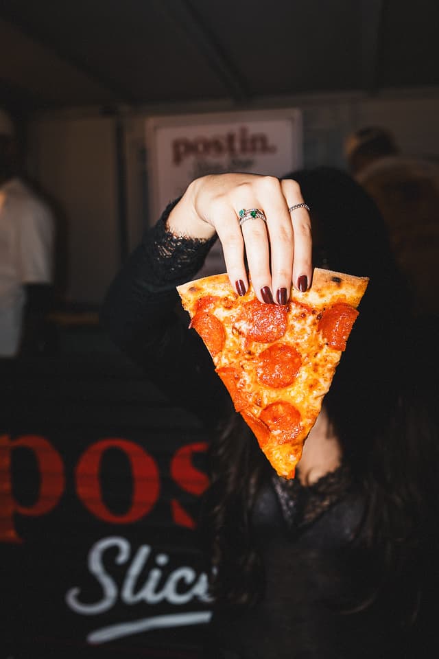 Convidada segurando uma fatia de pepperoni New York style no Postin Slice Shop